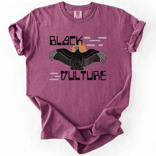 Berry "Black Vulture" t-shirt on Comfort Colors tee, featuring a vulture with spread wings against an orange sun with bold geometric lettering. Birdwatcher and scavenger lover gift shirt for wildlife and nature enthusiasts.