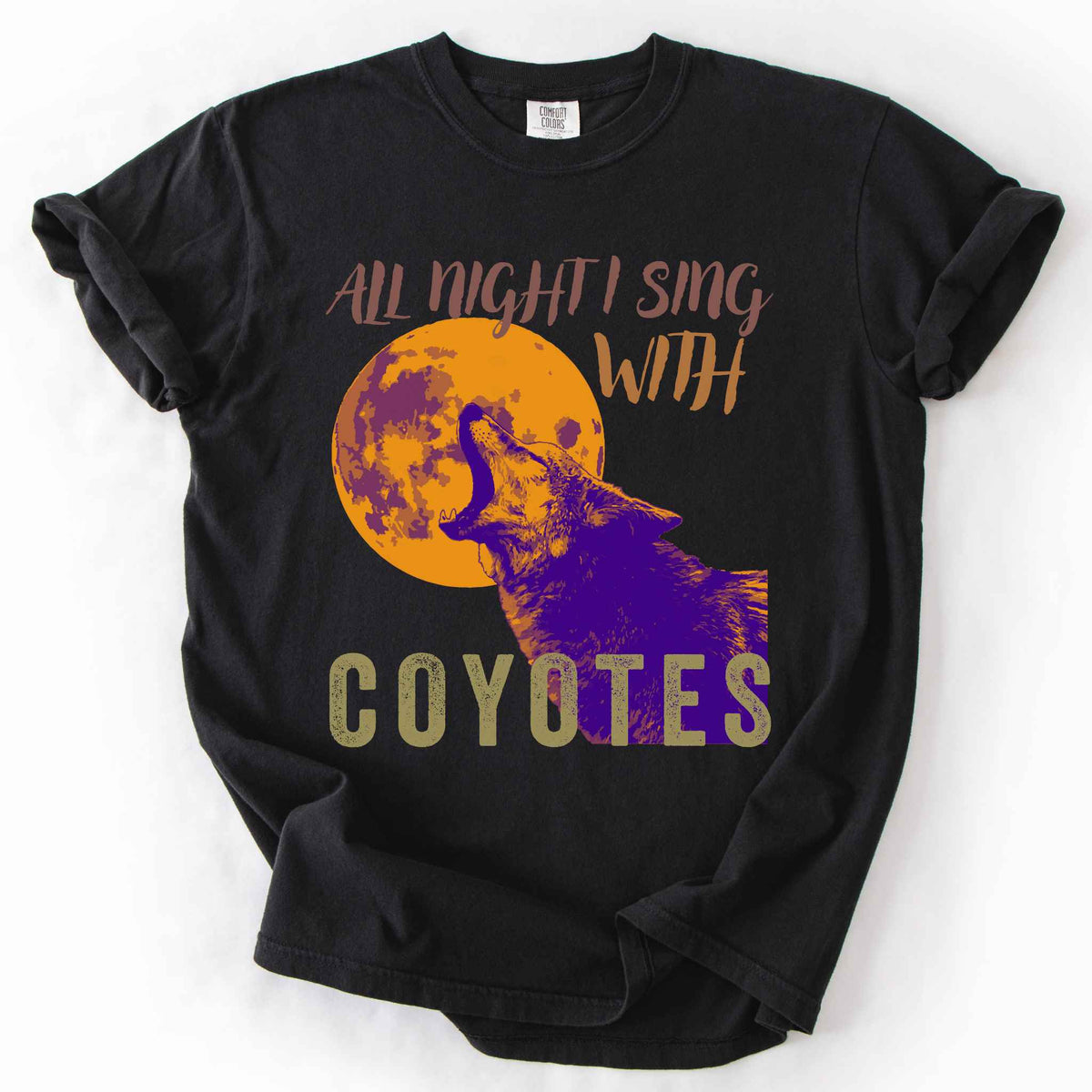 Black "All Night I Sing With Coyotes" t-shirt on Comfort Colors tee, featuring a purple and orange duotone graphic of a howling coyote against a full moon. Wildlife lover gift shirt for coyote and canid enthusiasts.
