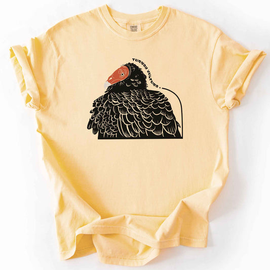 Butter "Turkey Vulture" t-shirt on Comfort Colors tee, featuring a bold illustrated portrait of a turkey vulture with a curved text label. Birdwatcher and scavenger lover gift shirt for wildlife and nature enthusiasts.
