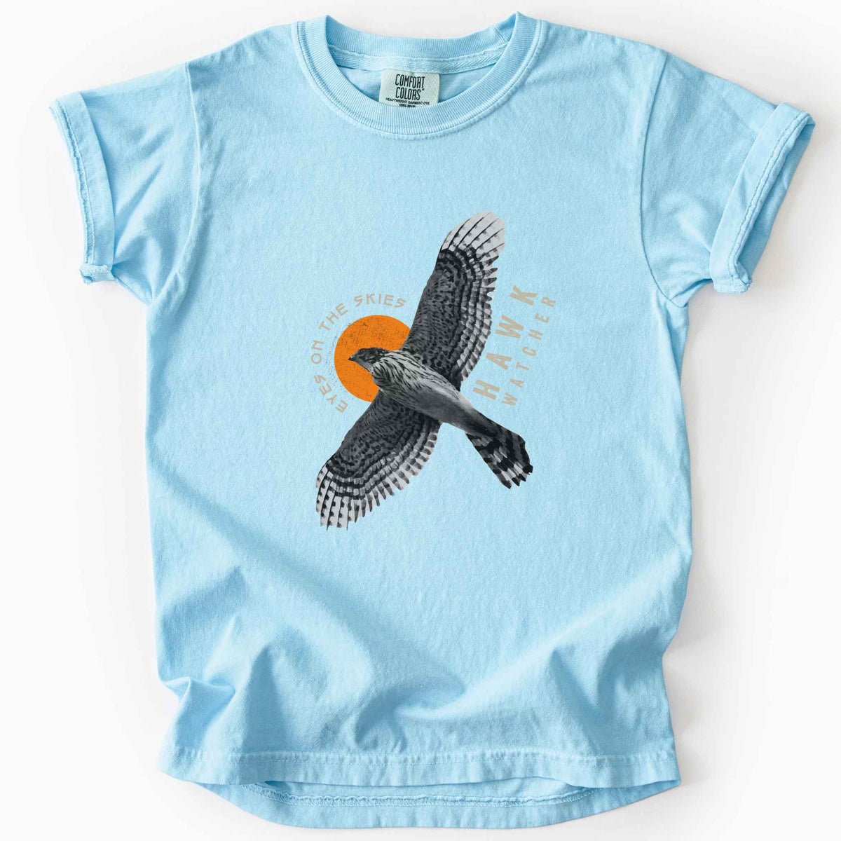 Chambray "Hawk Watcher, Eyes on the Skies" t-shirt on Comfort Colors tee, featuring a flying hawk graphic with spread wings against an orange sun design- birdwatching and raptor lover gift shirt for bird enthusiasts.