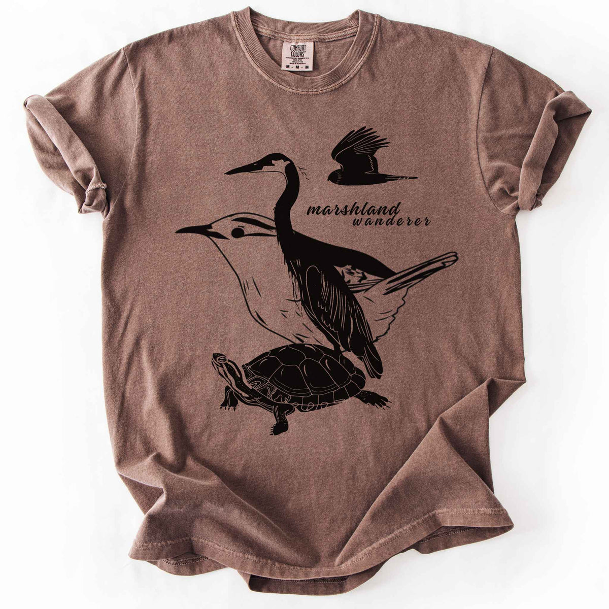 Espresso "Marshland Wanderer" t-shirt on Comfort Colors tee, featuring a surreal black line art design blending a heron, marsh wren, turtle, and marsh harrier into one flowing wetland scene. Nature lover and wetland conservation gift shirt for birdwatching and wildlife enthusiasts.