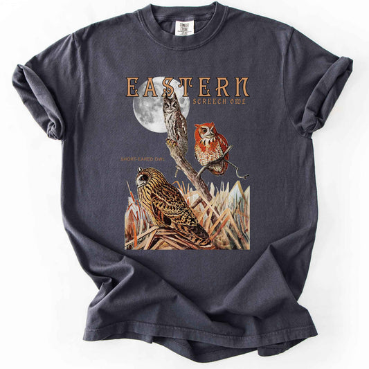 Graphite "Eastern Screech Owl" t-shirt on Comfort Colors tee, featuring a vintage style graphic of screech owls perched under a full moon with a short eared owl in the grass below. Birdwatcher and owl lover gift shirt for wildlife and nature enthusiasts.