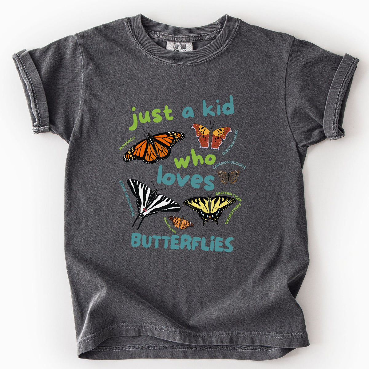 Pepper "Just a Kid Who Loves Butterflies" youth t-shirt on Comfort Colors tee, featuring six labeled butterfly species including Monarch, Zebra Swallowtail, and Painted Lady with playful green and teal lettering. Kids butterfly lover gift shirt for young nature explorers and budding entomologists.