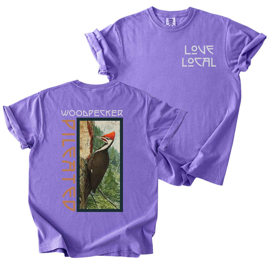 Violet "Pileated Woodpecker, Love Local" t-shirt on Comfort Colors tee, featuring a small front chest logo and a full vintage style back print of a woodpecker on a tree in a forest setting. Birdwatcher gift shirt for wildlife and nature enthusiasts.
