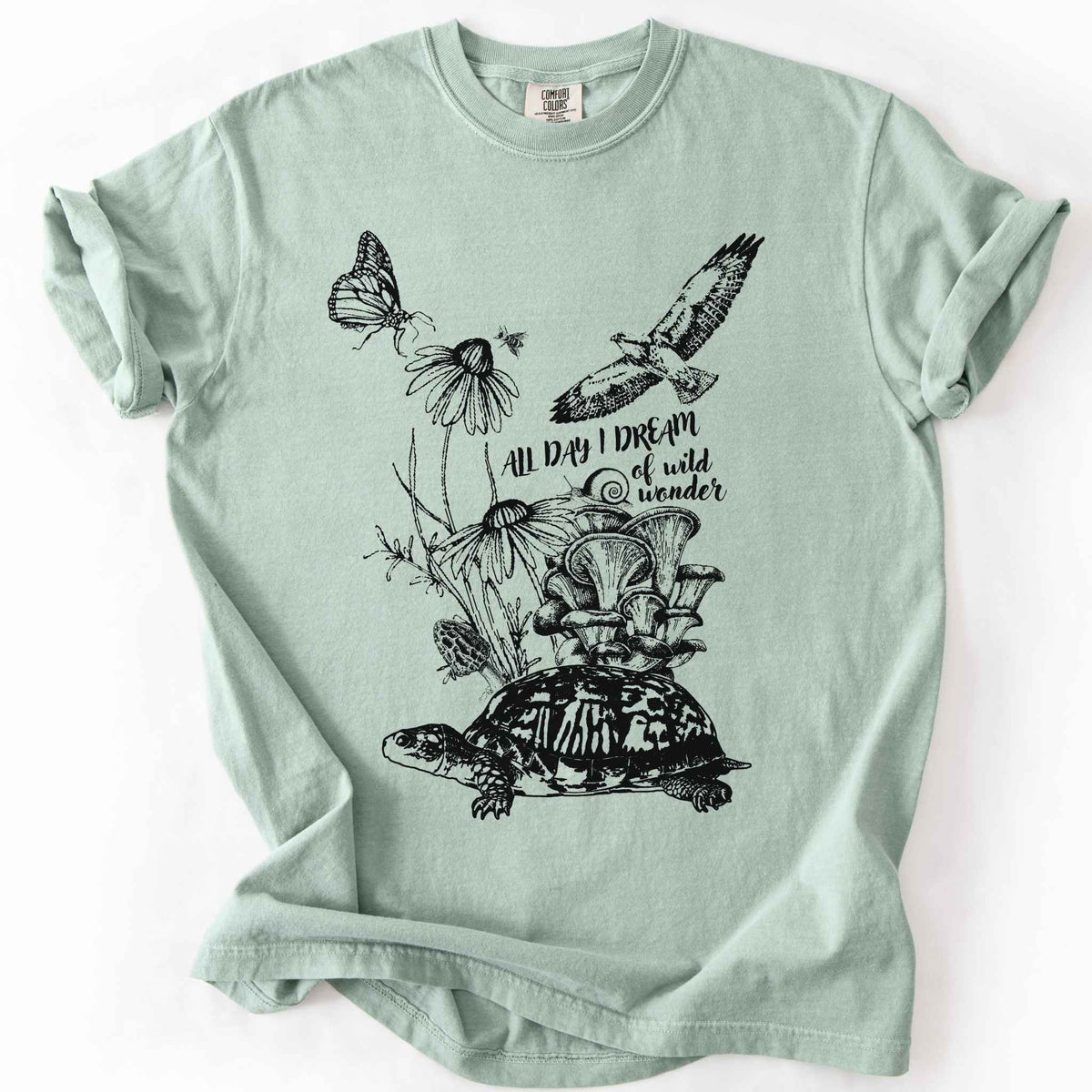 Bay "Fauna and Flora" t-shirt on Comfort Colors tee, featuring the words "all day I dream of wild wonder", and a nature scene in black line art style with a box turtle, mushrooms, wildflowers, a hawk, a butterfly, and a snail. Nature lover and forager gift shirt for cottagecore and wildlife enthusiasts.
