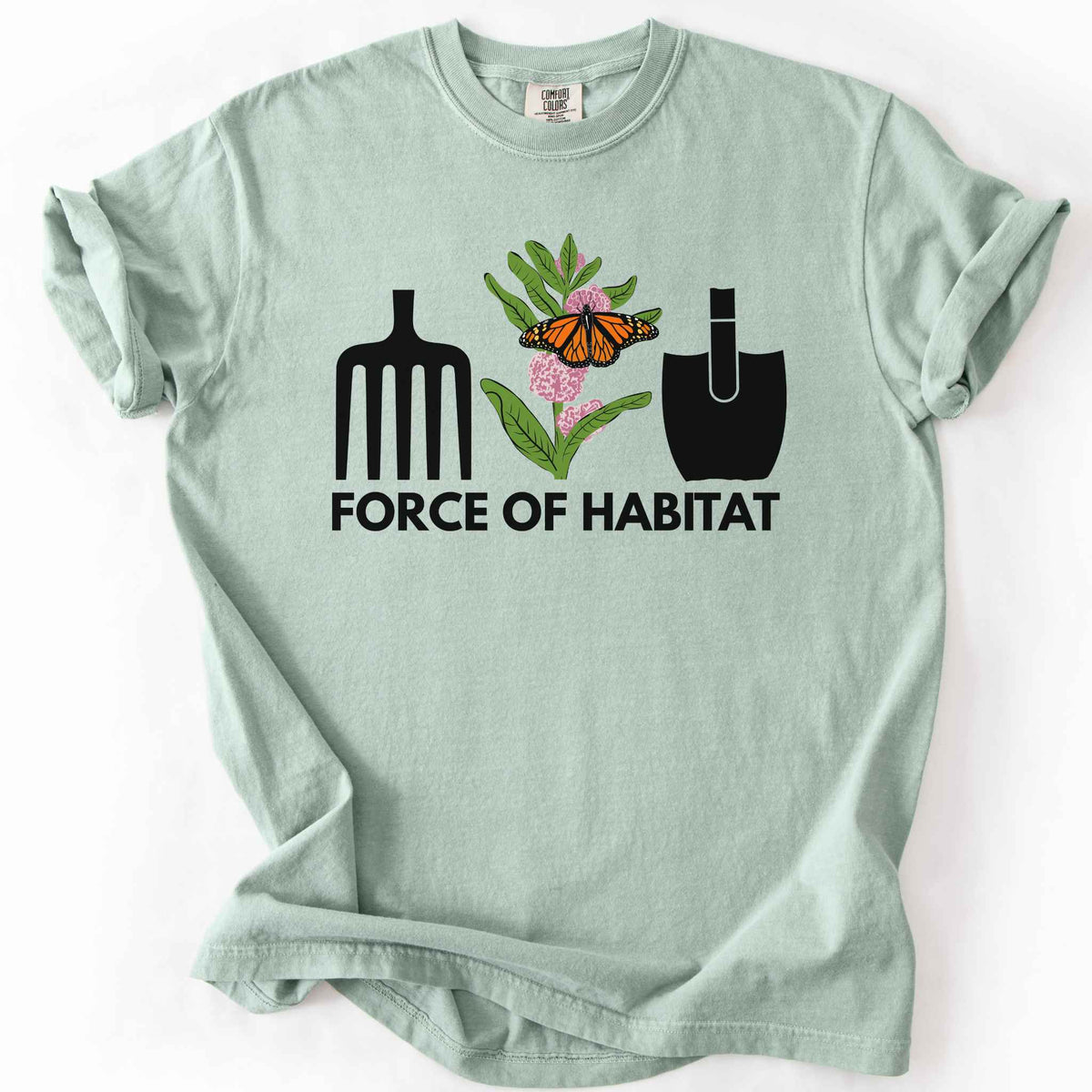 Bay "Force of Habitat: monarch" t-shirt on Comfort Colors tee, featuring garden tool graphics flanking a hand-drawn monarch butterfly on milkweed flowers with bold black text below. Gardener and native plant gift shirt for pollinator conservation fans.