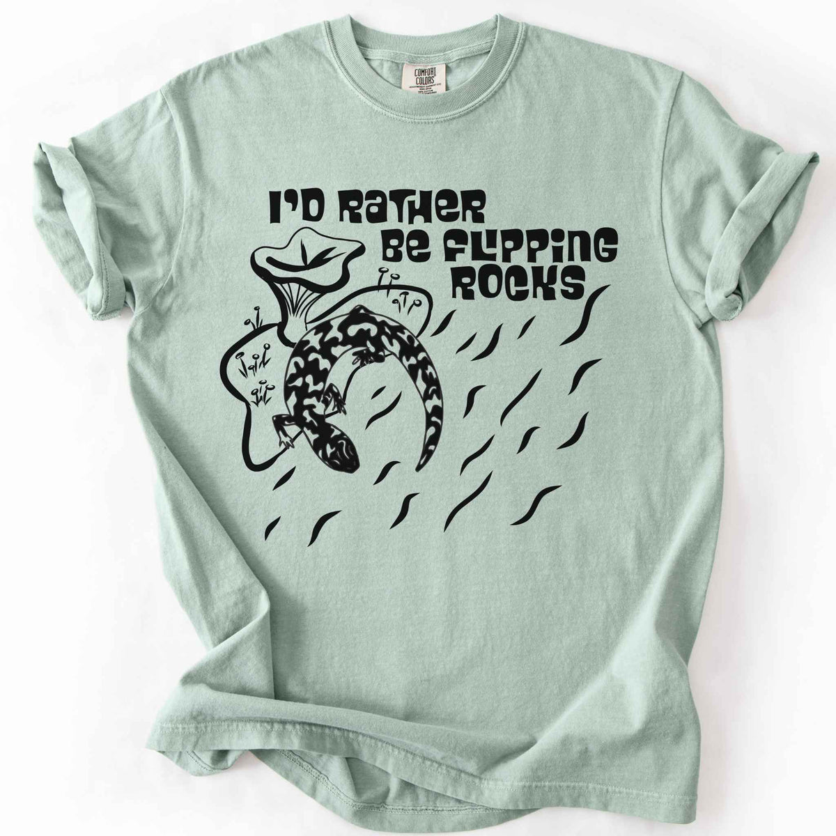 Bay "I'd Rather Be Flipping Rocks" t-shirt on Comfort Colors tee, featuring a bold graphic of a curled salamander with mushrooms in a groovy retro font. Funny herpetology gift shirt for salamander hunters and amphibian enthusiasts.