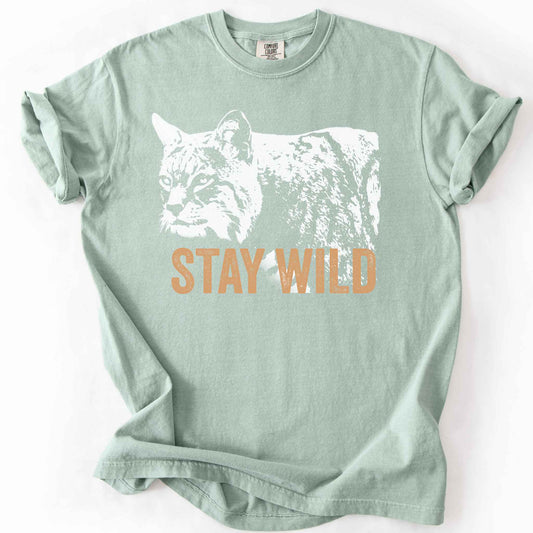 Bay "Stay Wild" t-shirt on Comfort Colors tee, featuring a bold white bobcat graphic with orange lettering — wildlife lover and nature enthusiast gift shirt for outdoorsy, animal-inspired style.