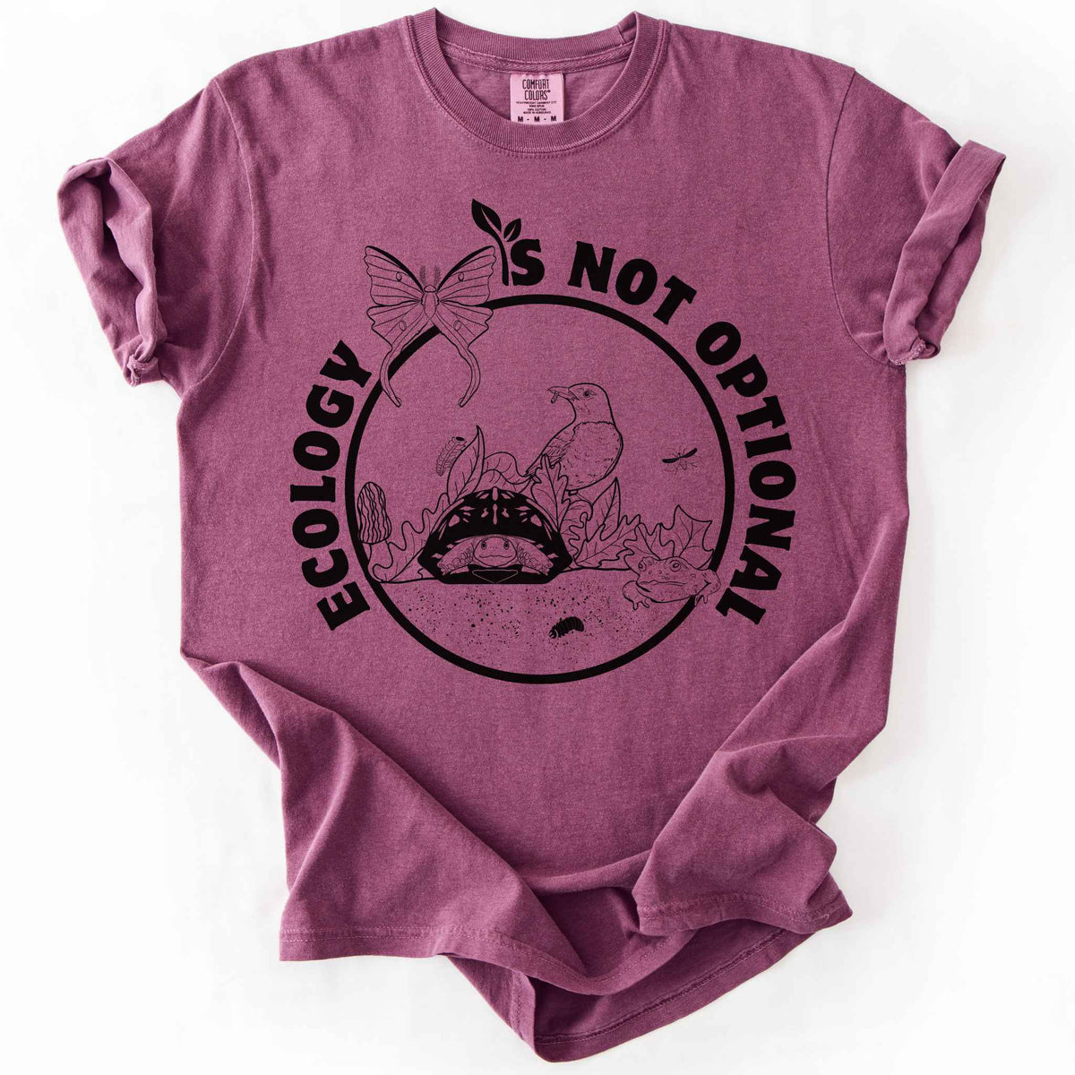 Berry "Ecology Is Not Optional" t-shirt on Comfort Colors tee, featuring a black circle badge with a box turtle, bird, luna moth, frog, and mushrooms in an ecosystem scene. Nature lover and biology gift shirt for ecologists and conservation enthusiasts.
