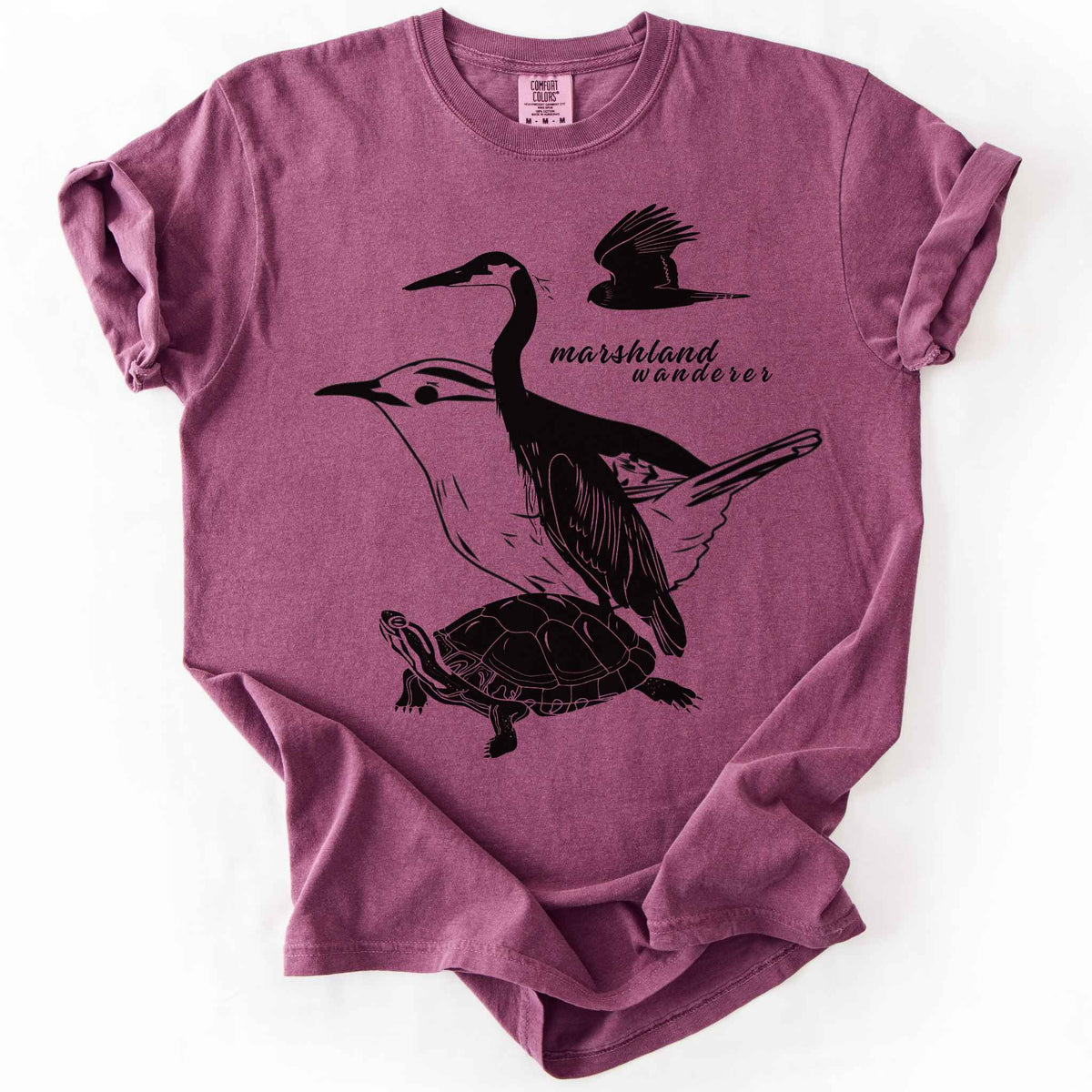 Berry "Marshland Wanderer" t-shirt on Comfort Colors tee, featuring a surreal black line art design blending a heron, marsh wren, turtle, and marsh harrier into one flowing wetland scene. Nature lover and wetland conservation gift shirt for birdwatching and wildlife enthusiasts.