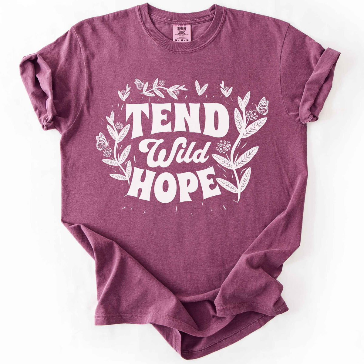 Berry "Tend Wild Hope" t-shirt on Comfort Colors tee, featuring hand drawn butterflies and milkweed flowers framing bold lettering. Gardener and native plant gift shirt for pollinator conservation and nature lovers.