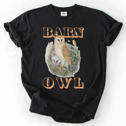 Black "Barn Owl" t-shirt on Comfort Colors tee, featuring a detailed graphic of a barn owl with owlets nestled in a tree hollow with ivy, in tan bold lettering. Birdwatcher and owl lover gift shirt for wildlife and nature enthusiasts.