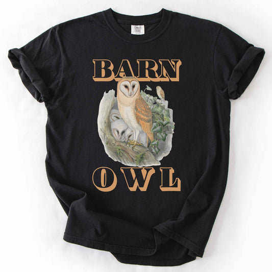 Black "Barn Owl" t-shirt on Comfort Colors tee, featuring a detailed graphic of a barn owl with owlets nestled in a tree hollow with ivy, in tan bold lettering. Birdwatcher and owl lover gift shirt for wildlife and nature enthusiasts.
