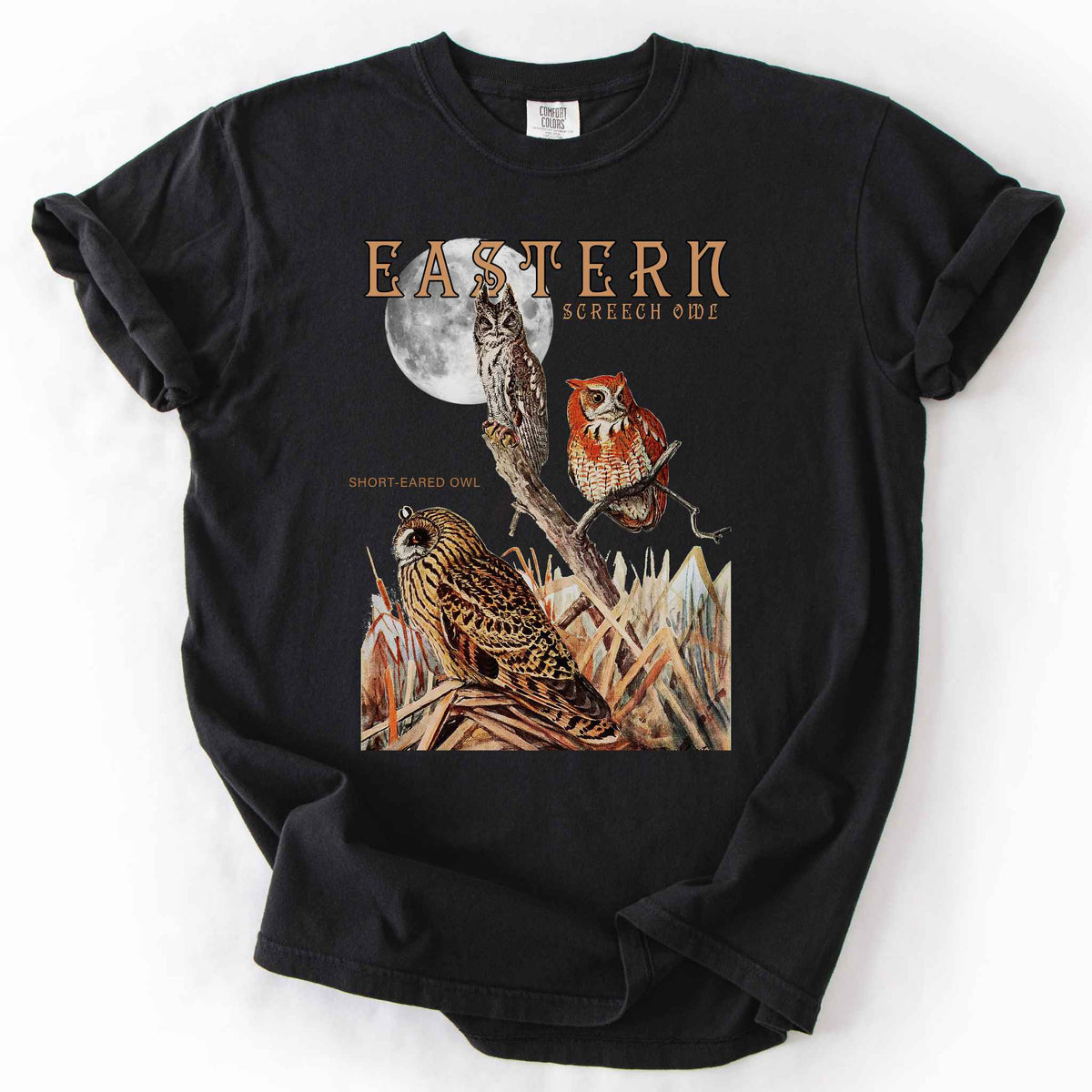 Black "Eastern Screech Owl" t-shirt on Comfort Colors tee, featuring a vintage style graphic of screech owls perched under a full moon with a short eared owl in the grass below. Birdwatcher and owl lover gift shirt for wildlife and nature enthusiasts.