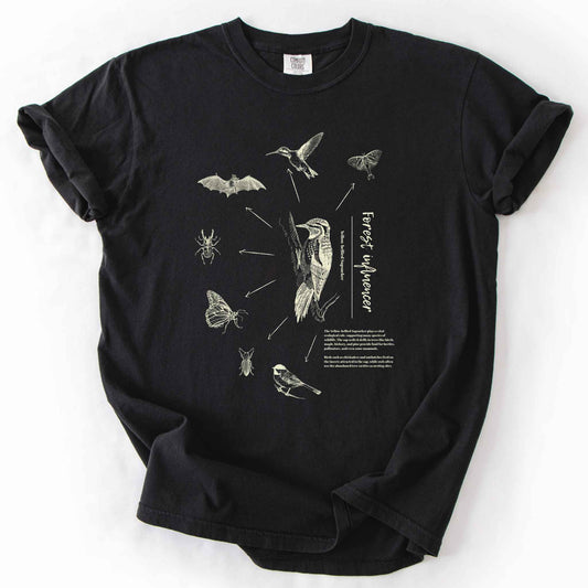 Black "Forest Influencer" t-shirt on Comfort Colors tee, featuring a vintage style Yellow bellied Sapsucker illustration surrounded by the beetles, moths, bats, and birds it supports, with educational text detailing its ecological role. Nature lover and birding gift shirt for wildlife and forest ecology fans.