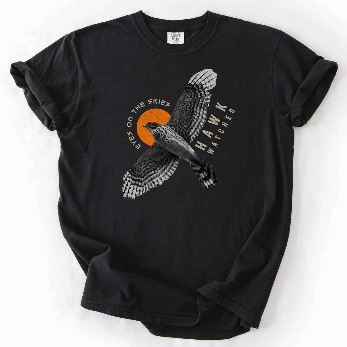Black "Hawk Watcher, Eyes on the Skies" t-shirt on Comfort Colors tee, featuring a flying hawk graphic with spread wings against an orange sun design- birdwatching and raptor lover gift shirt for bird enthusiasts.