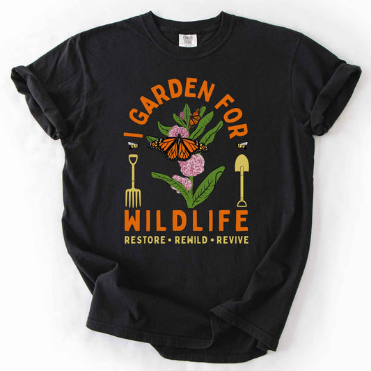 Black "I Garden for Wildlife, Restore, Rewild, Revive" t-shirt on Comfort Colors tee, featuring monarch butterflies and bees on milkweed flowers flanked by garden tools in orange and gold tones. Gardener and native plant gift shirt for pollinator conservation fans.