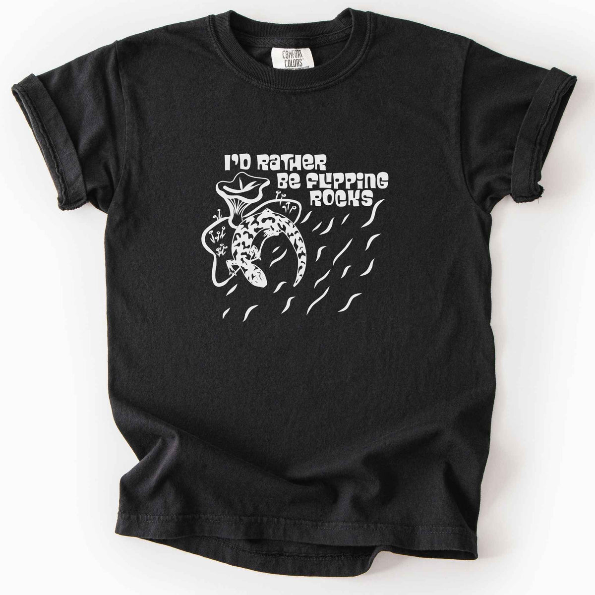Black "I'd Rather Be Flipping Rocks" kids t-shirt on Comfort Colors tee, featuring a bold graphic of a curled salamander with mushrooms in a groovy retro font. Funny herpetology gift shirt for salamander hunters and amphibian enthusiasts.