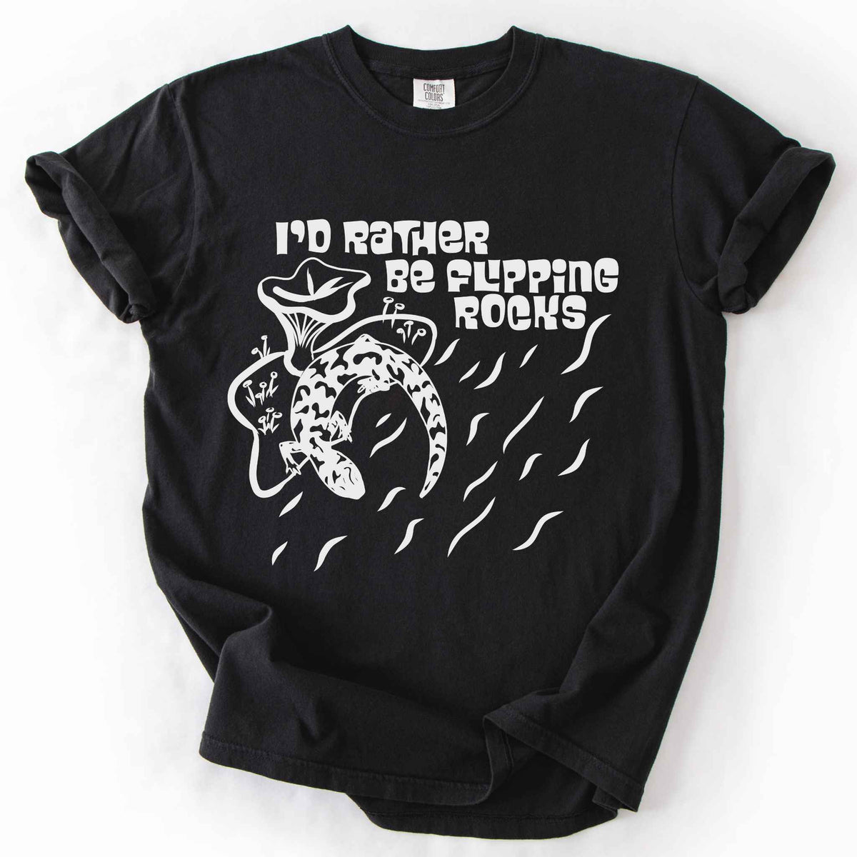 Black "I'd Rather Be Flipping Rocks" t-shirt on Comfort Colors tee, featuring a bold graphic of a curled salamander with mushrooms in a groovy retro font. Funny herpetology gift shirt for salamander hunters and amphibian enthusiasts.