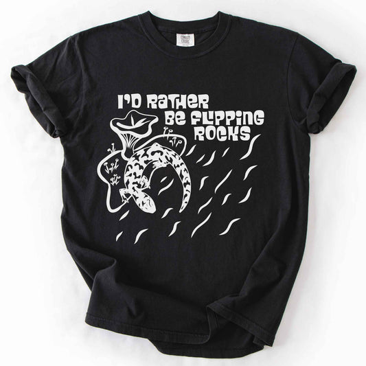 Black "I'd Rather Be Flipping Rocks" t-shirt on Comfort Colors tee, featuring a bold graphic of a curled salamander with mushrooms in a groovy retro font. Funny herpetology gift shirt for salamander hunters and amphibian enthusiasts.