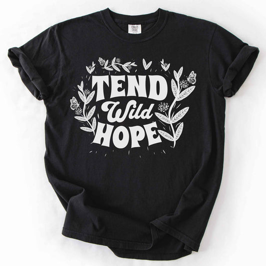 Black "Tend Wild Hope" t-shirt on Comfort Colors tee, featuring hand drawn butterflies and milkweed flowers framing bold lettering. Gardener and native plant gift shirt for pollinator conservation and nature lovers.