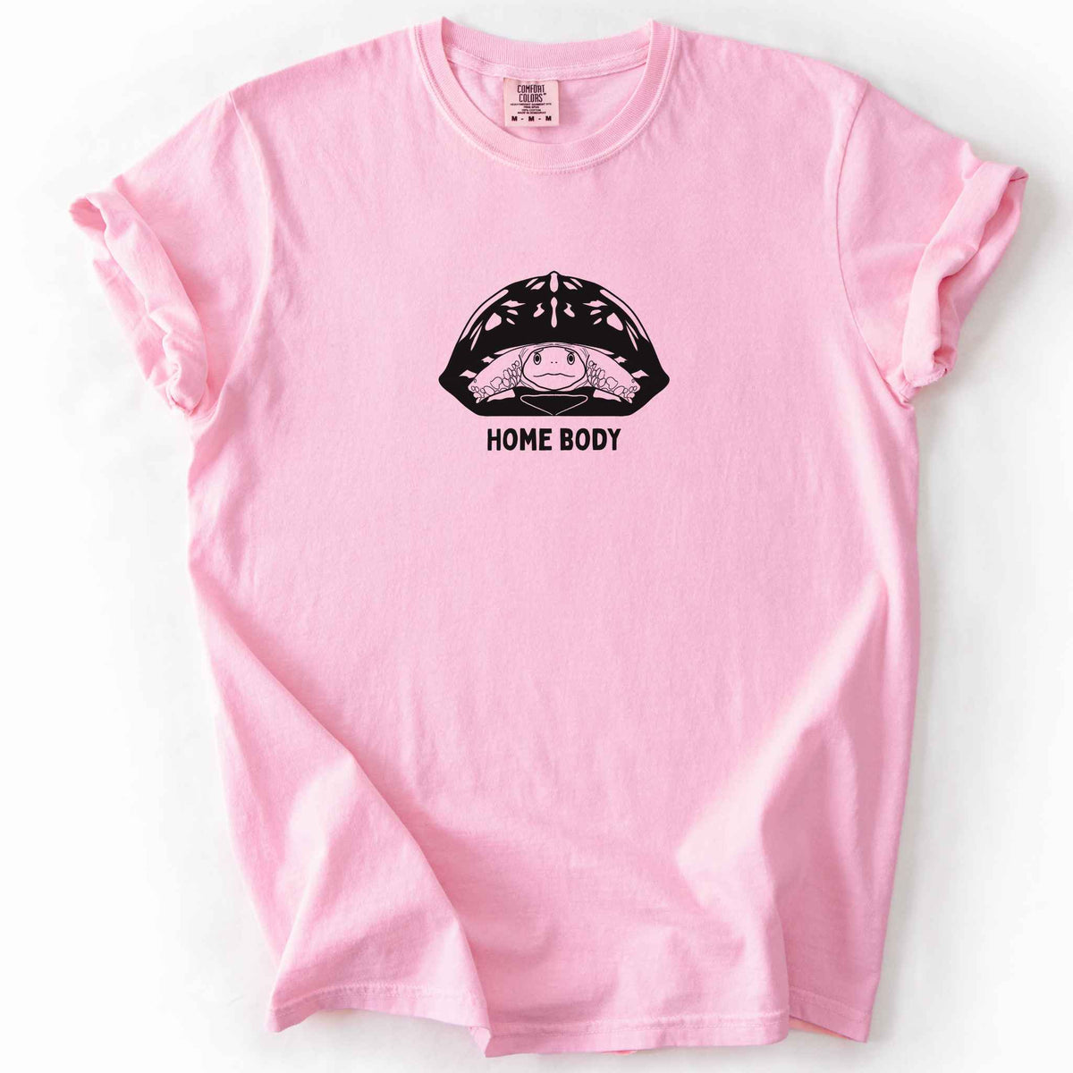 Blossom "Home Body" t-shirt on Comfort Colors tee, featuring a bold black graphic of a turtle peeking out from its shell above simple lettering. Funny turtle lover gift shirt for introverts and reptile enthusiasts.