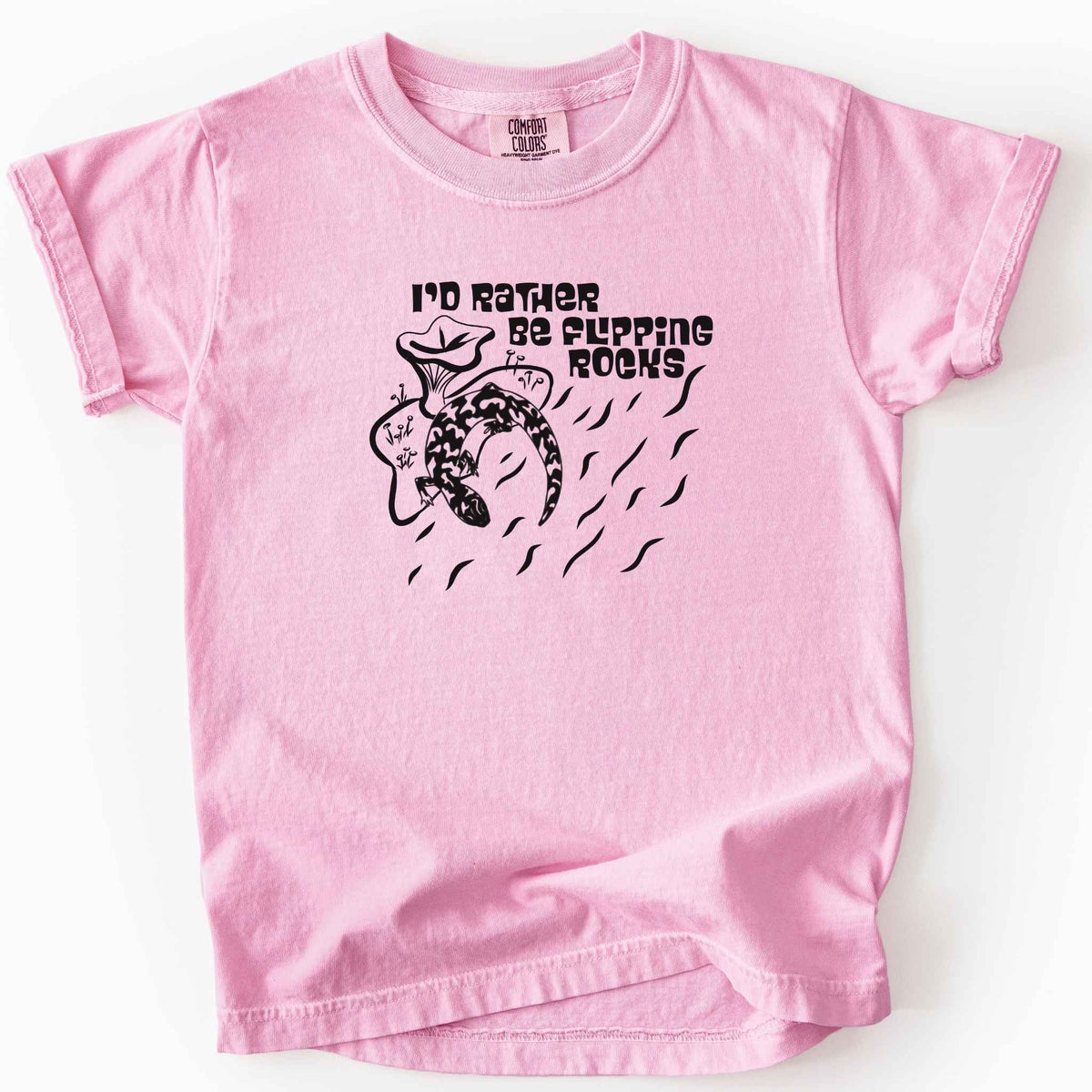 Blossom "I'd Rather Be Flipping Rocks" kids t-shirt on Comfort Colors tee, featuring a bold graphic of a curled salamander with mushrooms in a groovy retro font. Funny herpetology gift shirt for salamander hunters and amphibian enthusiasts.