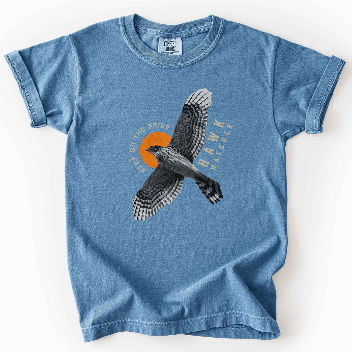 Blue Jean "Hawk Watcher, Eyes on the Skies" t-shirt on Comfort Colors tee, featuring a flying hawk graphic with spread wings against an orange sun design- birdwatching and raptor lover gift shirt for bird enthusiasts.
