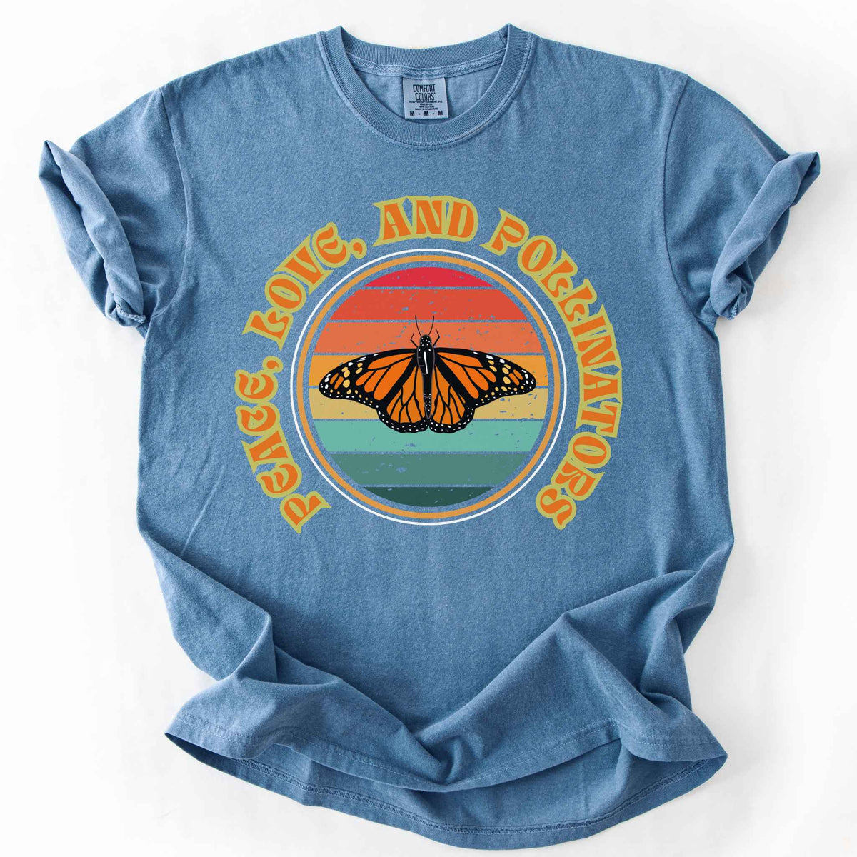 Blue Jean "Peace, Love, and Pollinators" t-shirt on Comfort Colors tee, featuring a monarch butterfly against a retro rainbow sunset circle design. Butterfly gardener and native plant gift shirt for pollinator conservation fans.
