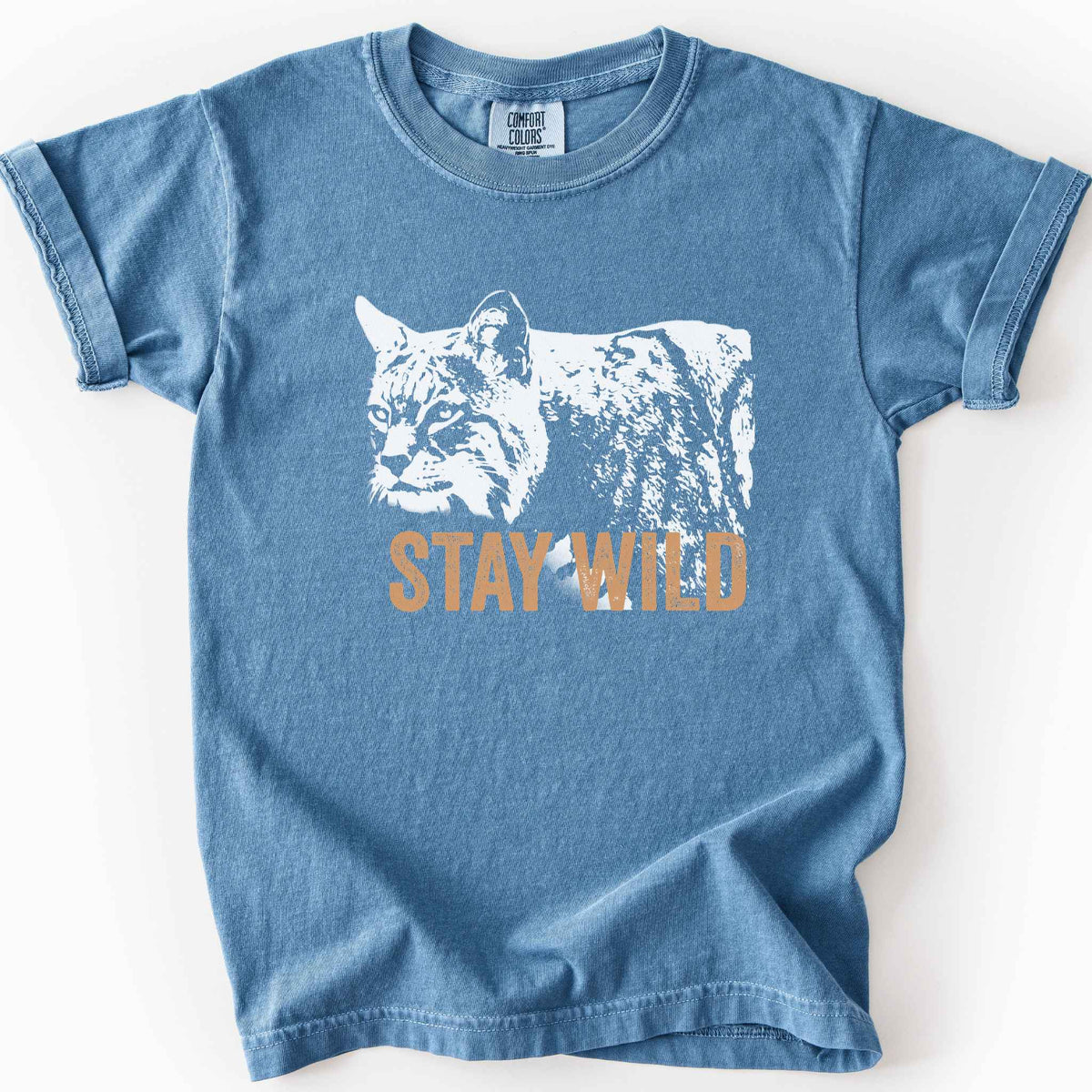 Blue Jean "Stay Wild" kids t-shirt on Comfort Colors tee, featuring a bold white bobcat graphic with orange lettering — wildlife lover and nature enthusiast gift shirt for outdoorsy, animal-inspired style.
