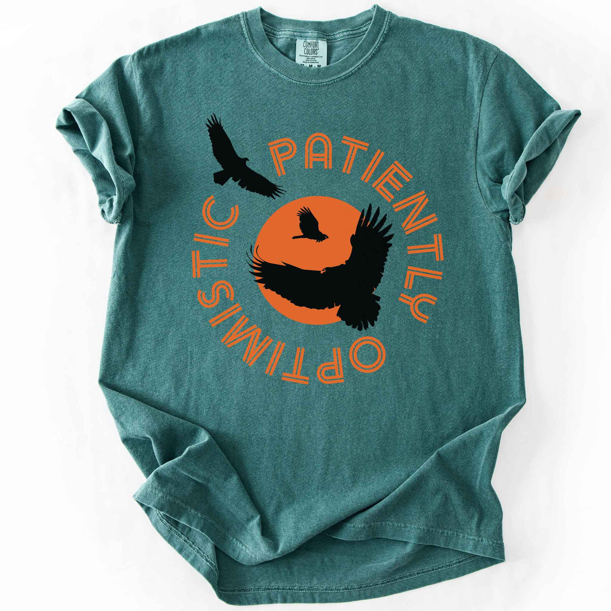 Blue Spruce "Patiently optimistic turkey vulture" t-shirt on comfort colors tee. Silhouette turkey vulture graphics against an orange sun surrounded by curved text. Bird lover and wildlife enthusiast gift. 