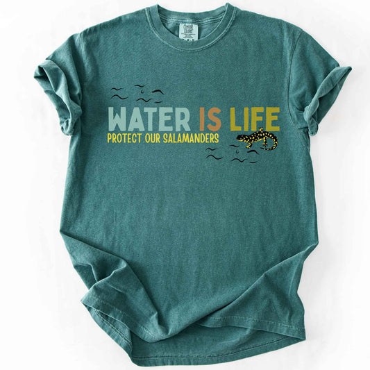 Blue Spruce "Water Is Life, Protect Our Salamanders" t-shirt on Comfort Colors tee, featuring a tiger salamander graphic with stylized water wave accents in teal, orange, and mustard text. Amphibian conservation gift shirt for salamander and wetland habitat lovers.