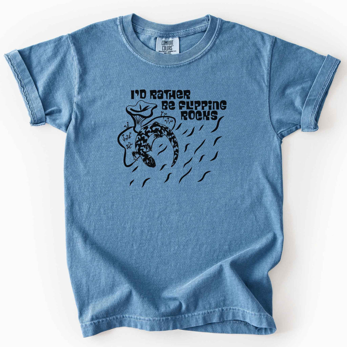 Blue jean "I'd Rather Be Flipping Rocks" kids t-shirt on Comfort Colors tee, featuring a bold graphic of a curled salamander with mushrooms in a groovy retro font. Funny herpetology gift shirt for salamander hunters and amphibian enthusiasts.