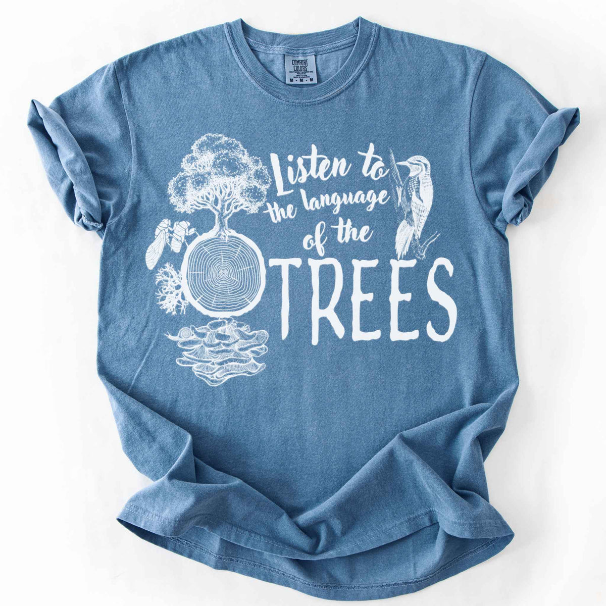 Blue jean "Listen to the Language of the Trees" t-shirt on Comfort Colors tee, featuring a tree, tree rings, woodpecker, cicada, and mushrooms in white. Nature lover and forest ecology gift shirt for tree huggers and outdoor enthusiasts.