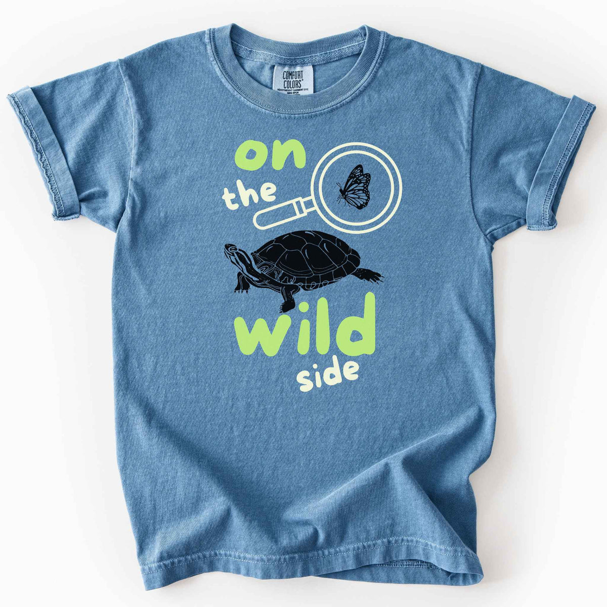 Blue jean "On the wild side" kids t-shirt on Comfort Colors tee featuring a butterfly in a magnifying glass and painted turtle graphic with bold and playful text. Nature lover kids shirt for wildlife and exploration enthusiasts. 