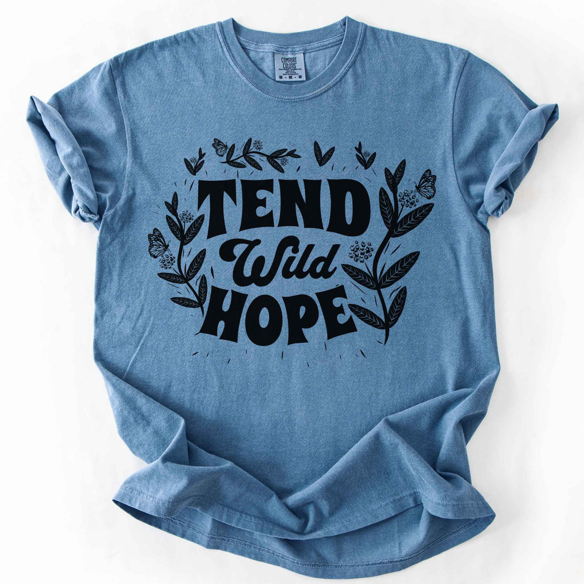 Blue jean "Tend Wild Hope" t-shirt on Comfort Colors tee, featuring hand drawn butterflies and milkweed flowers framing bold lettering. Gardener and native plant gift shirt for pollinator conservation and nature lovers.