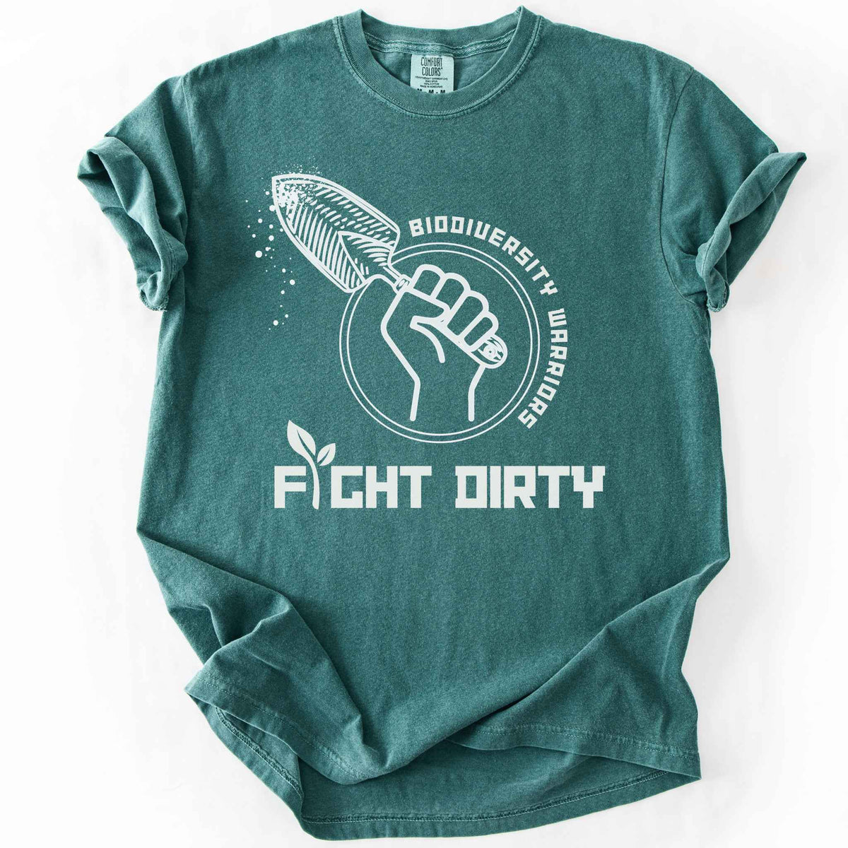 Blue spruce "Biodiversity Warriors, Fight Dirty" t-shirt on Comfort Colors tee, featuring a raised fist gripping a garden trowel in a circular badge design. Gardener and conservation lover gift shirt for native plant and biodiversity enthusiasts.
