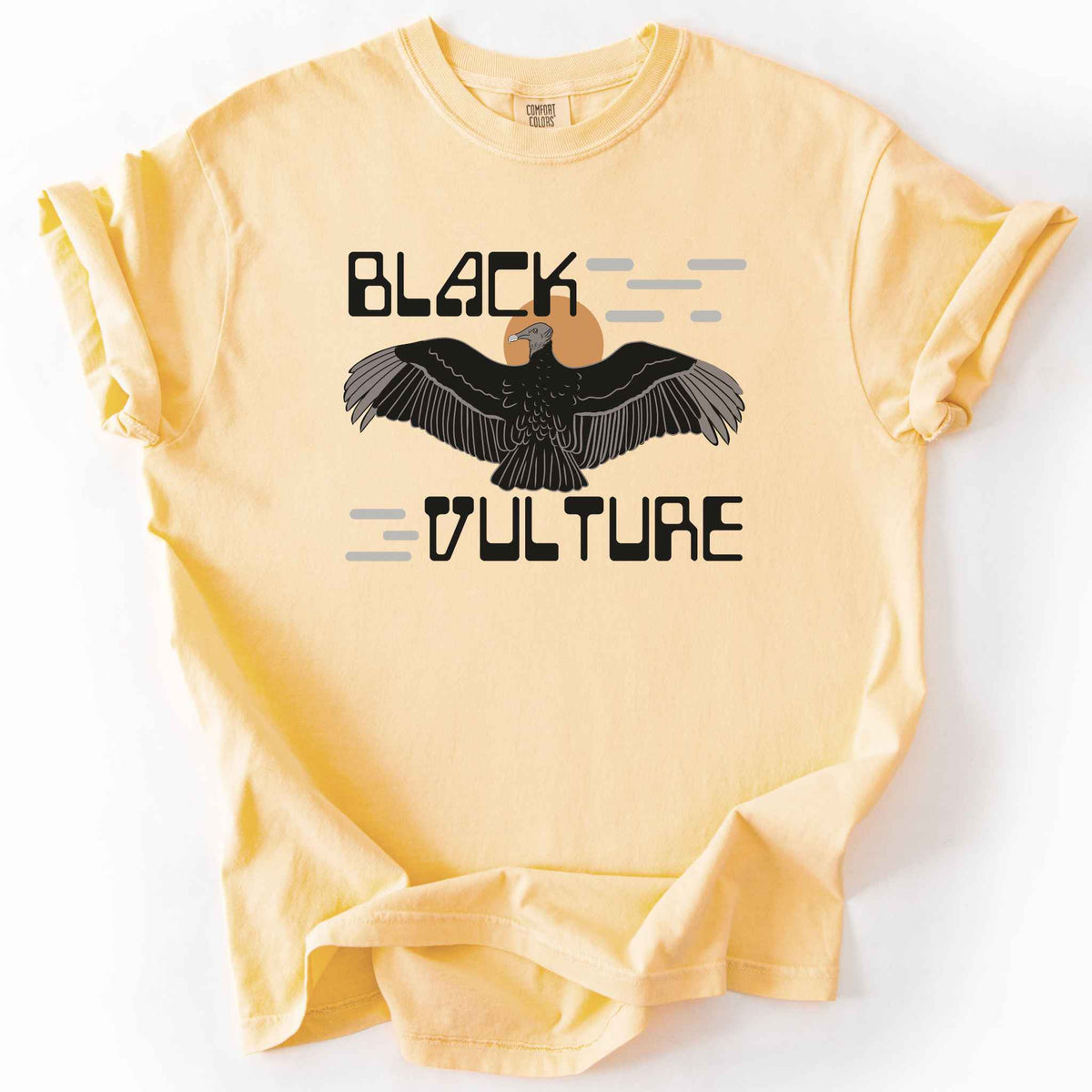 Butter "Black Vulture" t-shirt on Comfort Colors tee, featuring a vulture with spread wings against an orange sun with bold geometric lettering. Birdwatcher and scavenger lover gift shirt for wildlife and nature enthusiasts.