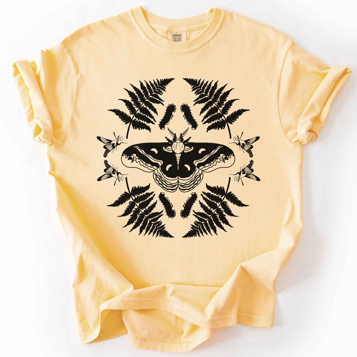 Butter "Cecropia moth" t-shirt on Comfort Colors tee, featuring a bold black symmetrical design of a moth surrounded by ferns and hummingbird moths in a mirrored botanical pattern. Nature lover and moth enthusiast gift shirt for entomology and cottagecore fans.