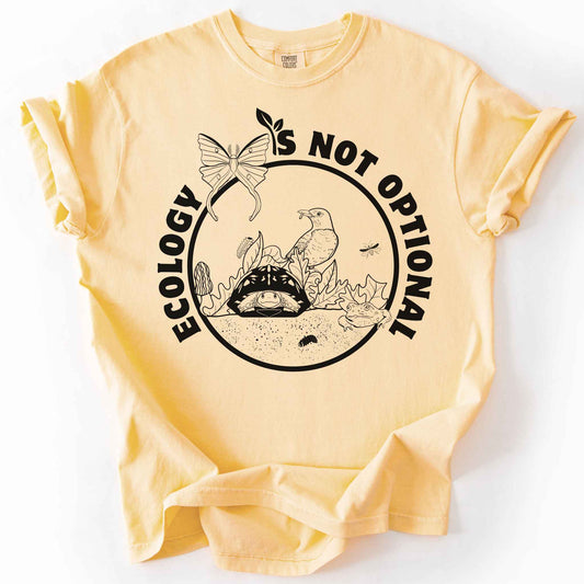 Butter "Ecology Is Not Optional" t-shirt on Comfort Colors tee, featuring a black circle badge with a box turtle, bird, luna moth, frog, and mushrooms in an ecosystem scene. Nature lover and biology gift shirt for ecologists and conservation enthusiasts.