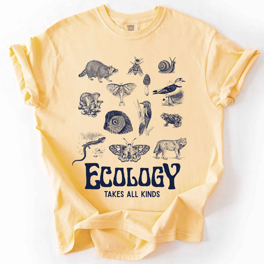 Butter "Ecology Takes All Kinds" t-shirt on Comfort Colors tee, featuring a grid of raccoons, owls, wolves, salamanders, mushrooms, moths, and other wildlife in cream ink. Nature lover and biology gift shirt for ecologists and wildlife enthusiasts.