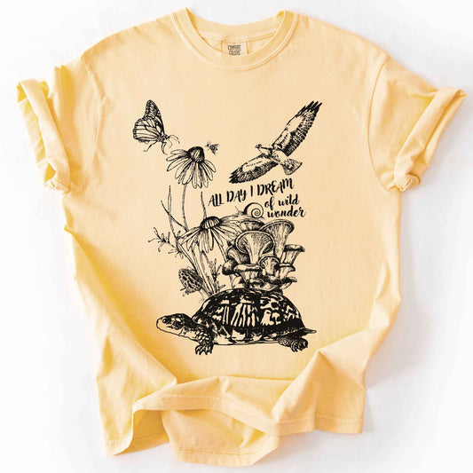 Butter "Fauna and Flora" t-shirt on Comfort Colors tee, featuring the words "all day I dream of wild wonder", and a nature scene in black line art style with a box turtle, mushrooms, wildflowers, a hawk, a butterfly, and a snail. Nature lover and forager gift shirt for cottagecore and wildlife enthusiasts.