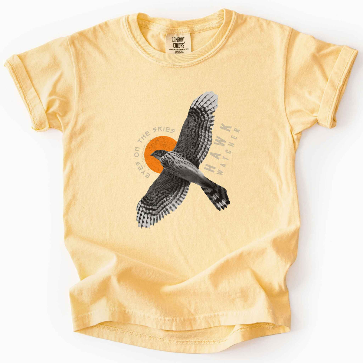 Butter "Hawk Watcher, Eyes on the Skies" t-shirt on Comfort Colors tee, featuring a flying hawk graphic with spread wings against an orange sun design- birdwatching and raptor lover gift shirt for bird enthusiasts.