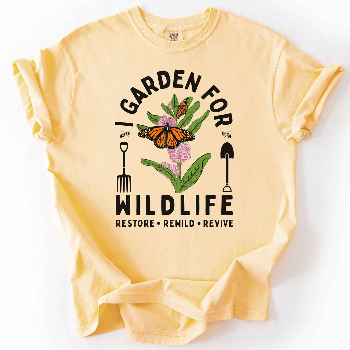 Butter "I Garden for Wildlife, Restore, Rewild, Revive" t-shirt on Comfort Colors tee, featuring monarch butterflies and bees on milkweed flowers flanked by garden tools in orange and gold tones. Gardener and native plant gift shirt for pollinator conservation fans.