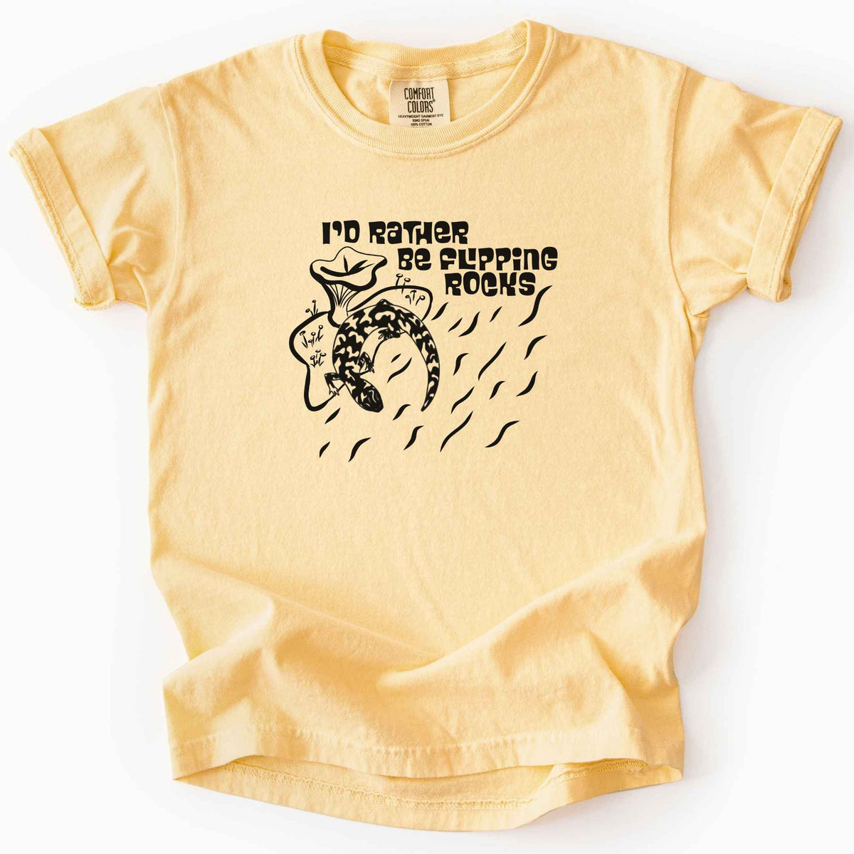 Butter "I'd Rather Be Flipping Rocks" kids t-shirt on Comfort Colors tee, featuring a bold graphic of a curled salamander with mushrooms in a groovy retro font. Funny herpetology gift shirt for salamander hunters and amphibian enthusiasts.
