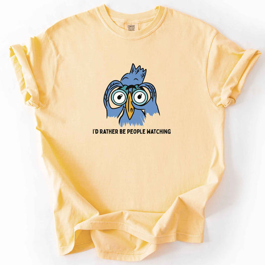 Butter "I'd Rather Be People Watching" t-shirt on Comfort Colors tee, featuring a cartoon blue bird holding binoculars up to its eyes. Funny birdwatcher gift shirt for bird lovers and introverts.
