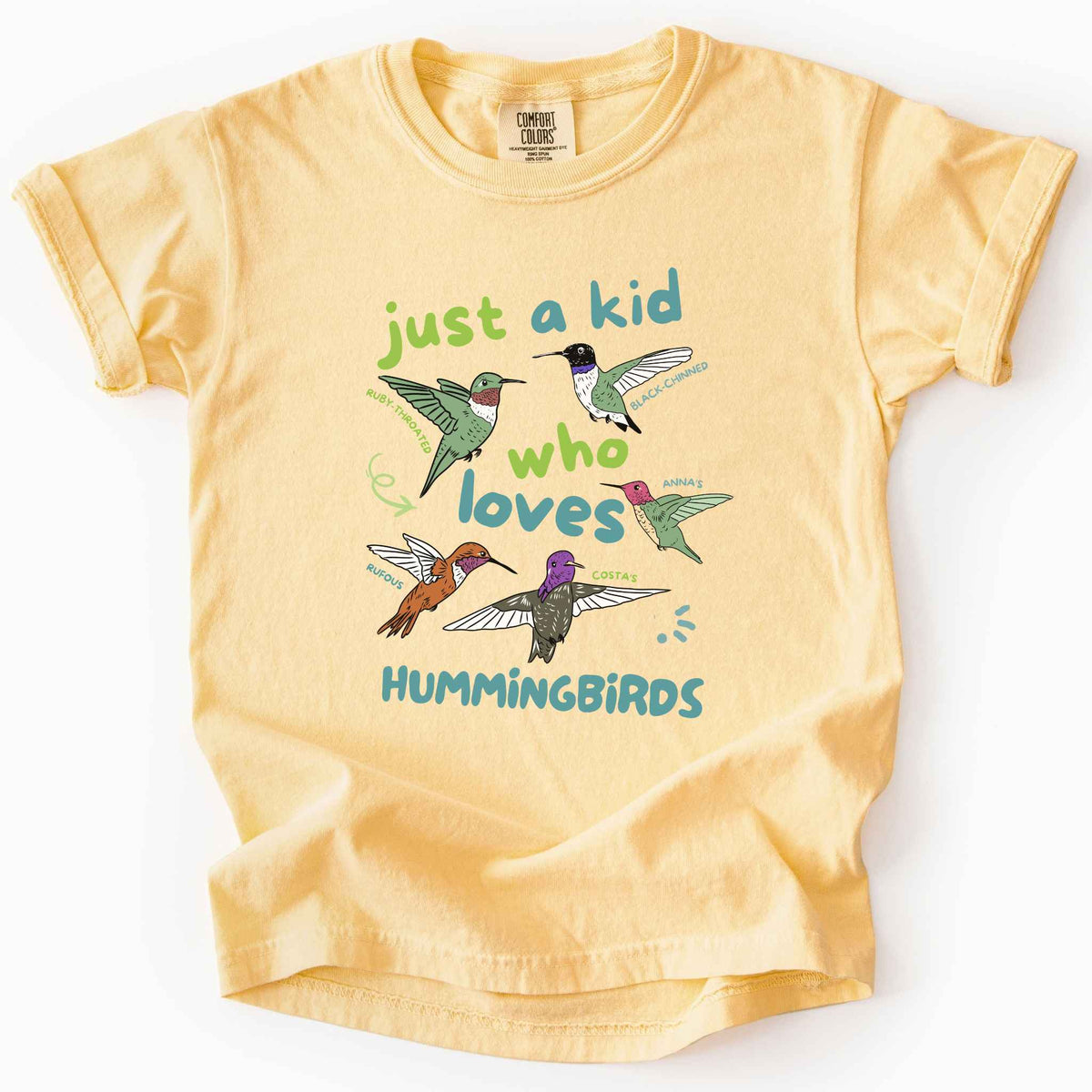 Butter "Just a Kid Who Loves Hummingbirds" youth t-shirt on Comfort Colors tee, featuring five labeled hummingbird species including Ruby Throated, Anna's, and Costa's with playful green and blue lettering. Kids birdwatcher gift shirt for young nature lovers and budding wildlife enthusiasts.