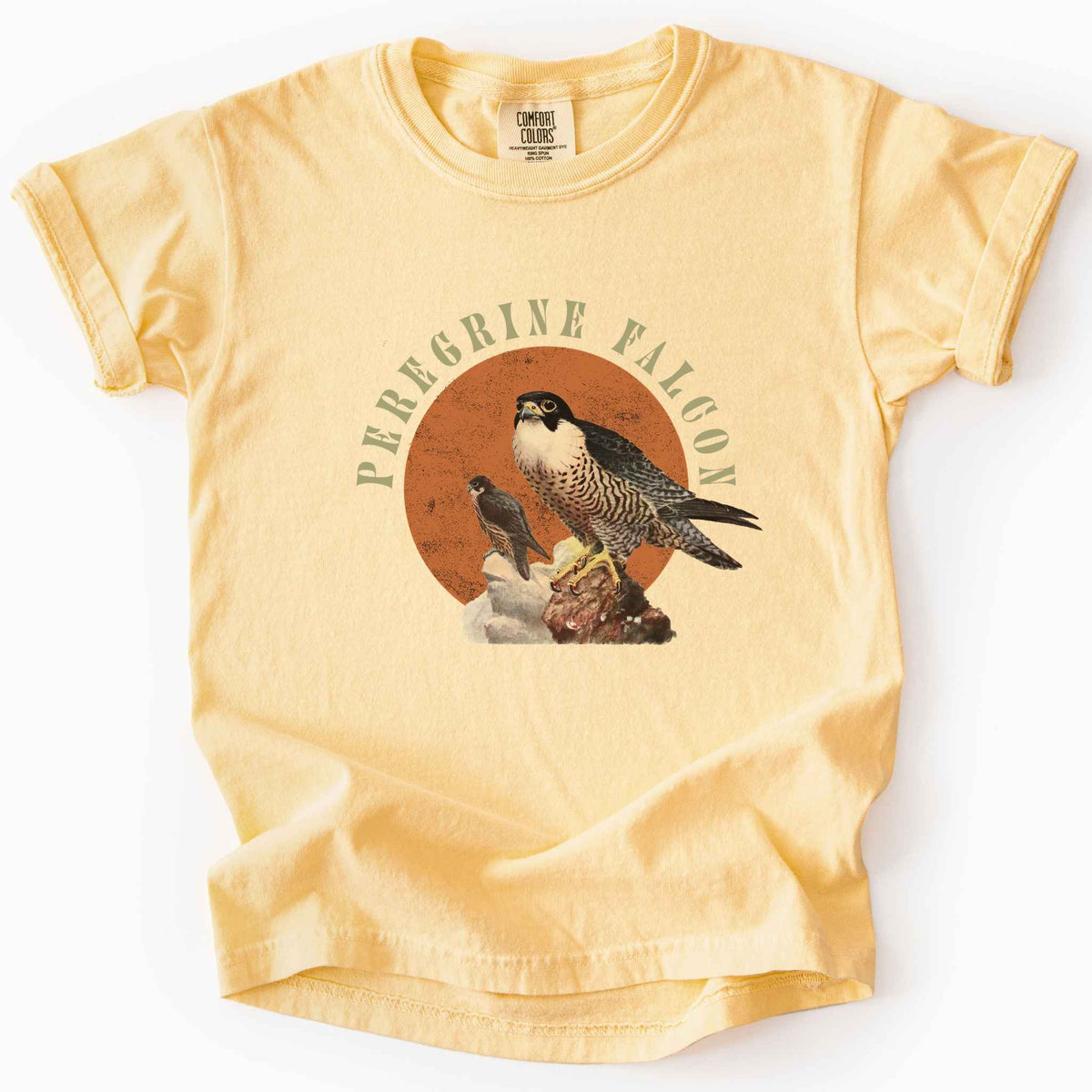 Butter "Peregrine Falcon" kids t-shirt on Comfort Colors tee, featuring vintage style falcon illustration perched on a rock against an orange sun backdrop, with arched cream text. Birdwatcher and raptor lover gift shirt for falconry and wildlife fans.