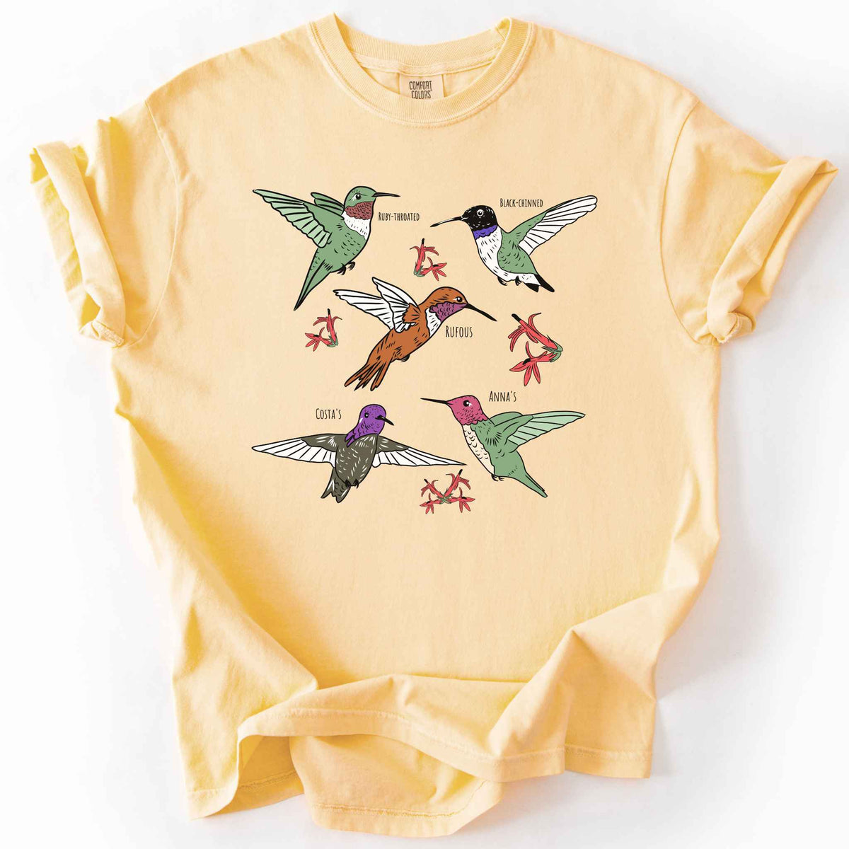 Butter "hummingbirds" t-shirt on Comfort Colors tee, featuring five illustrated hummingbird species including Ruby Throated, Rufous, and Anna's, each labeled and shown among red flowers. Birdwatcher and hummingbird lover gift shirt for wildlife and nature enthusiasts.