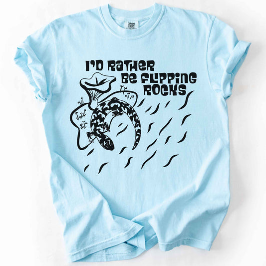 Chalky Mint "I'd Rather Be Flipping Rocks" t-shirt on Comfort Colors tee, featuring a bold graphic of a curled salamander with mushrooms in a groovy retro font. Funny herpetology gift shirt for salamander hunters and amphibian enthusiasts.